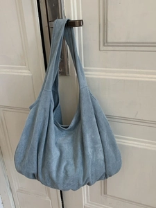 Blue suede oversized tote bag with casual pleated design hanging on a white door
