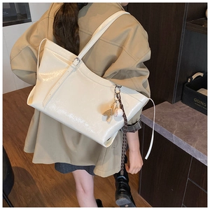 Detail of cream glossy leather tote bag with stylish baseball charm on the shoulder strap