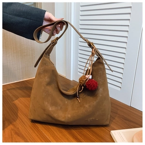 Detail einer braunen Wildleder-Hobo-Tasche mit verstellbarem Gurt und MERFIL-Prägelogo