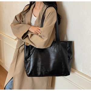Close-up of black glossy leather tote bag with MOCOBAG embossed logo carried by a model