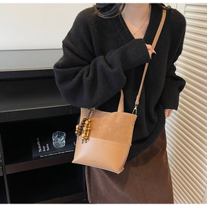 Detail of a brown suede and leather bucket bag with wooden bead charm and gold buckle