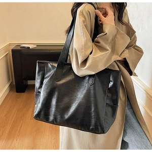 Model wearing a large black PU leather tote bag with embossed logo and textured finish