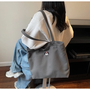 Close-up of a large grey canvas tote bag with a cute dog embroidery shown on a shoulder