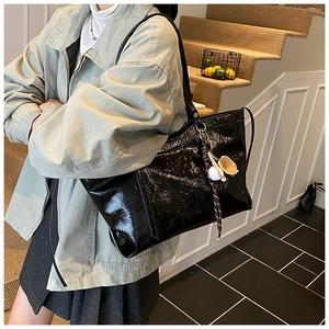 Close-up of black patent leather tote bag with creative baseball glove charm