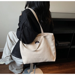 Close-up of a cream canvas tote bag featuring cute dog embroidery on a model shoulder