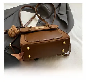 Details des braunen Lederrucksacks mit goldenen Bodenfüßen und Teddybär-Anhänger