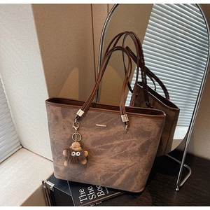 Brown suede tote bag with metal bar detail and plush monster charm on black surface