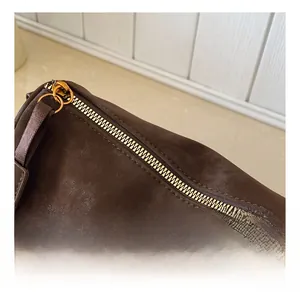 Gros plan sur la fermeture éclair dorée et le daim de ce sac polochon marron foncé