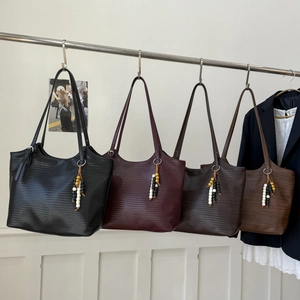 Détail de quatre sacs cabas tressés en noir, bordeaux et marron avec breloques perlées