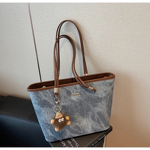 Close-up of denim blue tote bag with brown leather trim and plush monster charm decoration