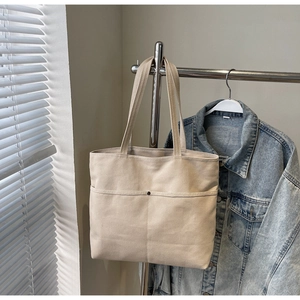 Detail of a large beige canvas tote bag with front pockets on an indoor hanger