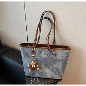 Detail of vintage denim tote bag with brown leather handles and plush monster charm