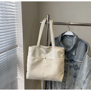 Detail showing the spacious front pocket and metal rivets on the ivory canvas tote bag