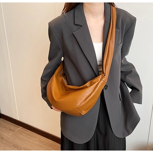 Detailed view of the caramel brown crescent bag worn as a shoulder bag on a grey blazer