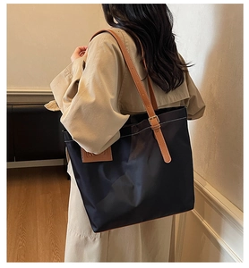 Side view of large black tote bag with brown straps worn with a beige trench coat