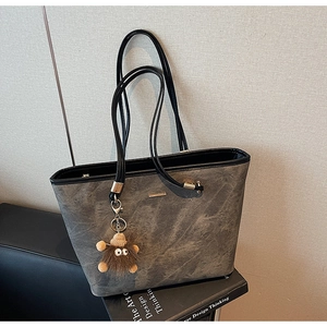 Detail of grey textured tote bag featuring a gold metal bar and a plush monster charm