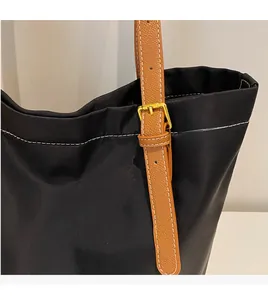 Detail of black nylon tote bag featuring brown leather straps with white stitching