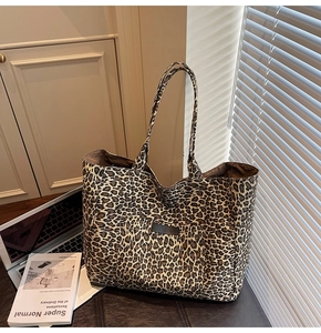Detail of leopard print canvas tote bag featuring front pocket on a leather surface