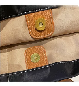 Detail shot of a secure gold magnetic clasp on a black nylon tote bag with leather trim