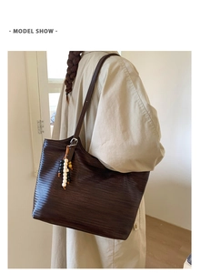 Detail of dark brown woven tote bag with wooden bead charm worn with a trench coat