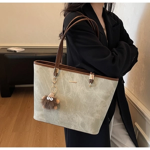Grey-green tote bag with marble texture, brown leather handles and plush monster charm