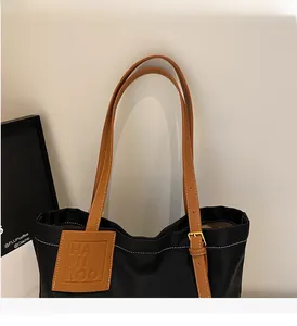 Detail of black tote bag featuring brown leather straps and adjustable gold buckles