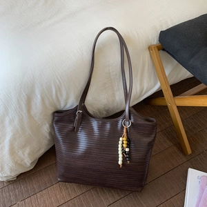 Gros plan d'un sac cabas tressé marron foncé avec un détail de pompon en perles de bois