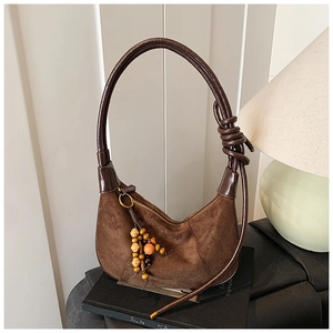 Detail of a brown suede crescent bag featuring a rope strap and colorful wooden bead charm
