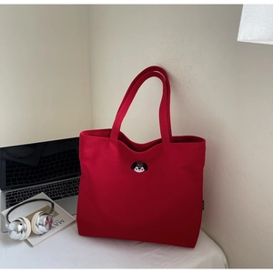 Close-up of red canvas tote bag with cartoon dog embroidery in a lifestyle desktop setup