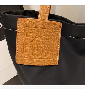 Detail of black nylon tote featuring brown lychee grain leather patch and logo