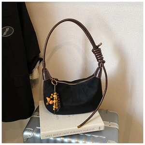 Detail of black suede crescent bag with brown knotted strap and colorful beaded charm