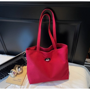 Detail of red canvas tote bag with dog embroidery beside a laptop and books