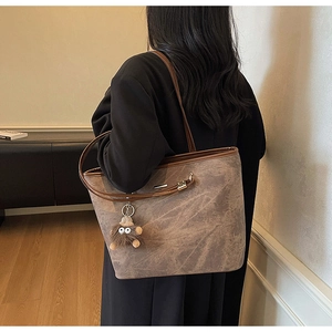 Detailed side view of large earth-tone tote bag with stone pattern and plush charm