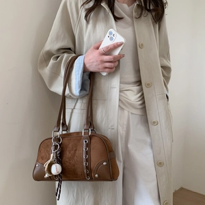 Detailed side view of vintage brown suede shoulder bag with baseball charm and metal eyelets