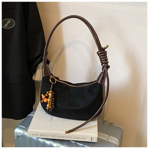 Detail of black suede crescent bag with knotted brown strap and beaded charm on luggage