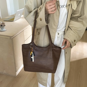 Brown woven texture tote bag detail with colorful beaded tassel shown in a lifestyle setting