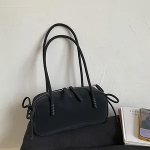 Détail du sac polochon noir mat avec de fines lanières et des nœuds décoratifs sur les côtés