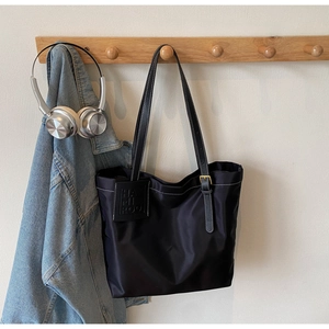Detail of black nylon tote bag with white contrast stitching and gold metal hardware