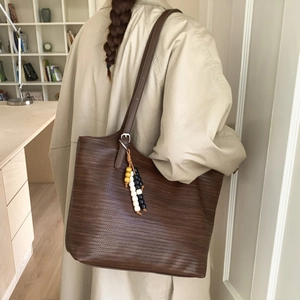 Detail of deep brown woven leather tote bag with colorful beaded charm and silver buckle