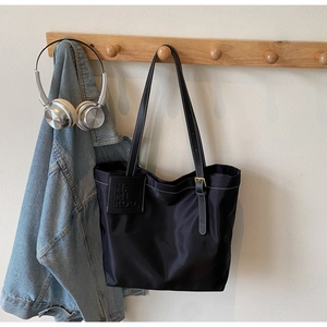 Detail of black tote bag with white contrast stitching and branded leather tag