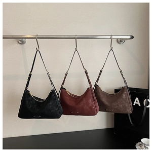 Three minimalist suede hobo bags in black, burgundy and brown hanging on a metal rack