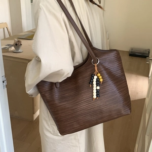 Detail of dark brown tote bag featuring woven texture and a stylish beaded tassel charm