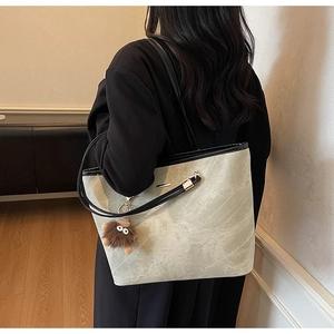 Detail of light grey marble pattern tote bag with black handles and plush monster charm
