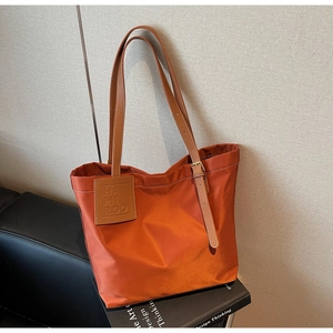 Detailed view of the caramel orange nylon tote bag with leather straps and logo tag