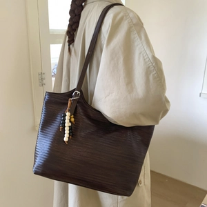 Detail view of brown woven tote bag featuring a wooden bead charm and adjustable strap