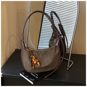 Detail of olive green suede hobo bag with wooden bead charm against a cozy home interior