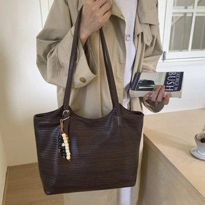 Detail of dark brown woven tote bag featuring a decorative beaded tassel and slim shoulder strap
