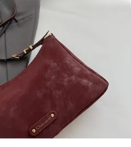 Detail of burgundy suede shoulder bag showing metal brand plate and soft texture