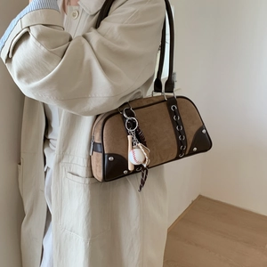 Close-up of brown suede underarm bag featuring metal studs and a baseball glove charm