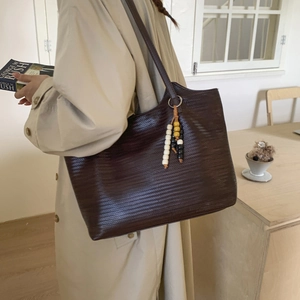 Detail of dark brown woven tote bag with fringe charm and long shoulder strap